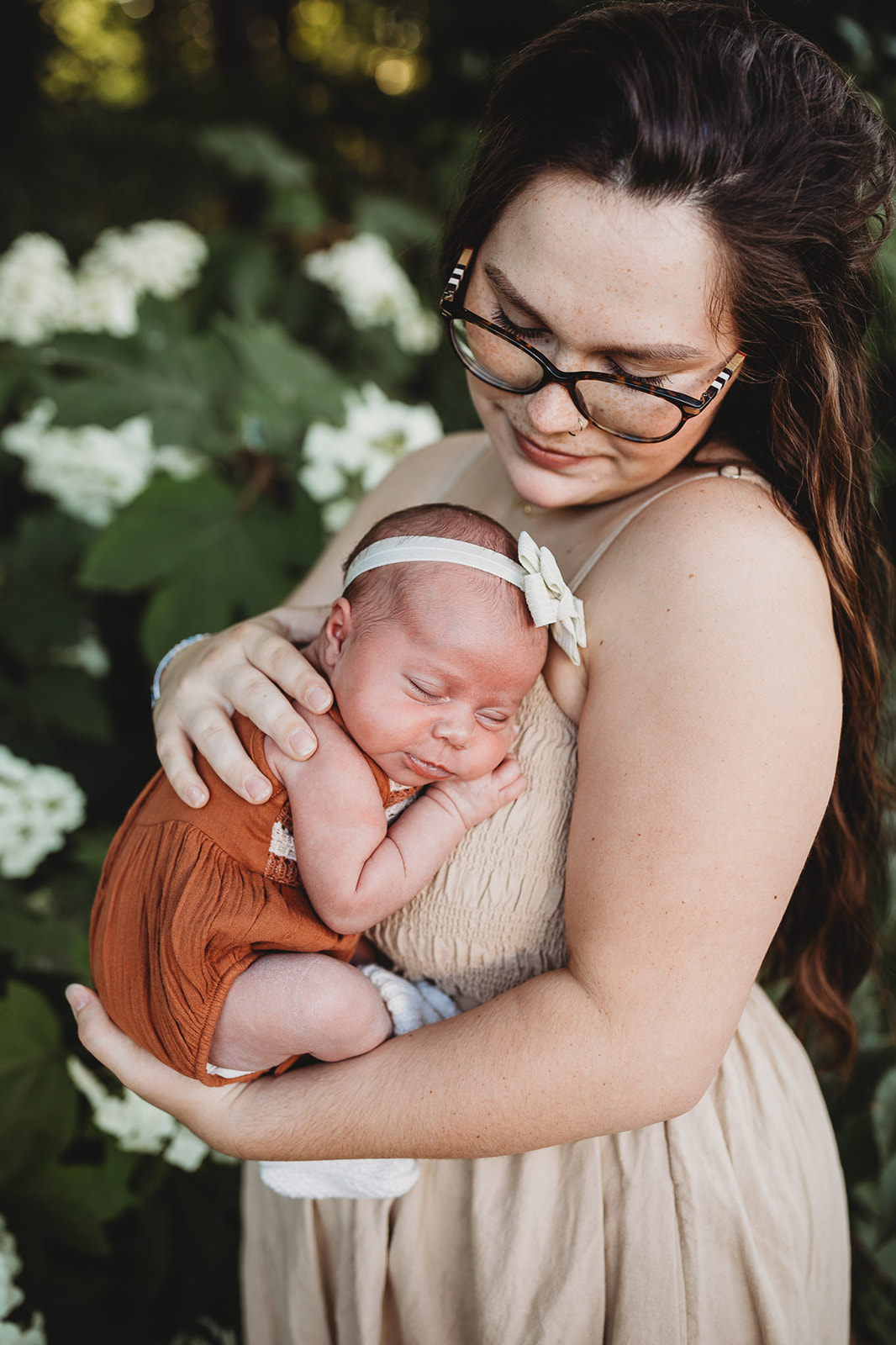 A happy mom cradles her sleeping infant daughter against her chest in a garden with white flowers after a 3D Ultrasound Harrisonburg, VA