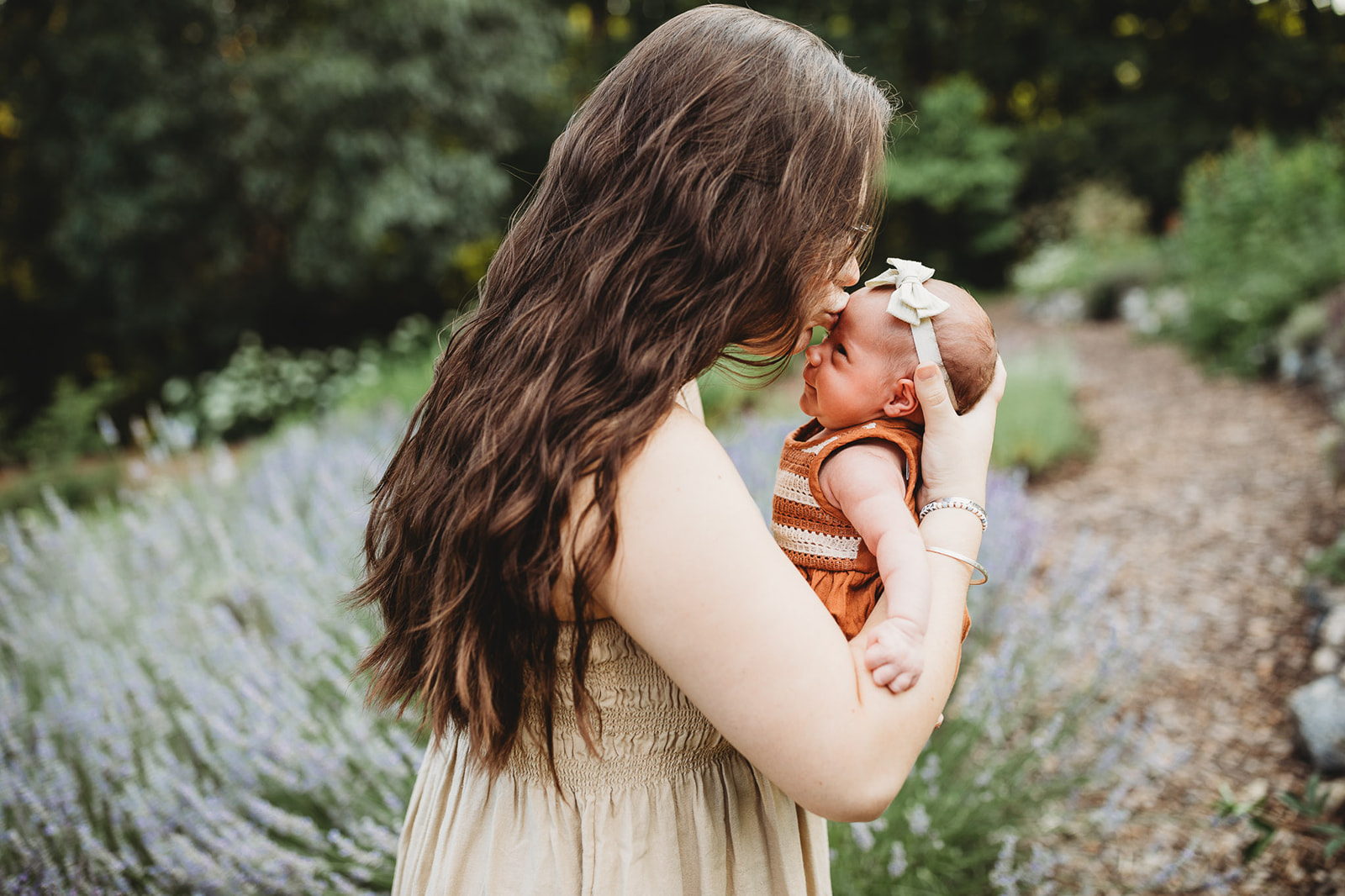 A new mom kisses her infant while standing in a park garden