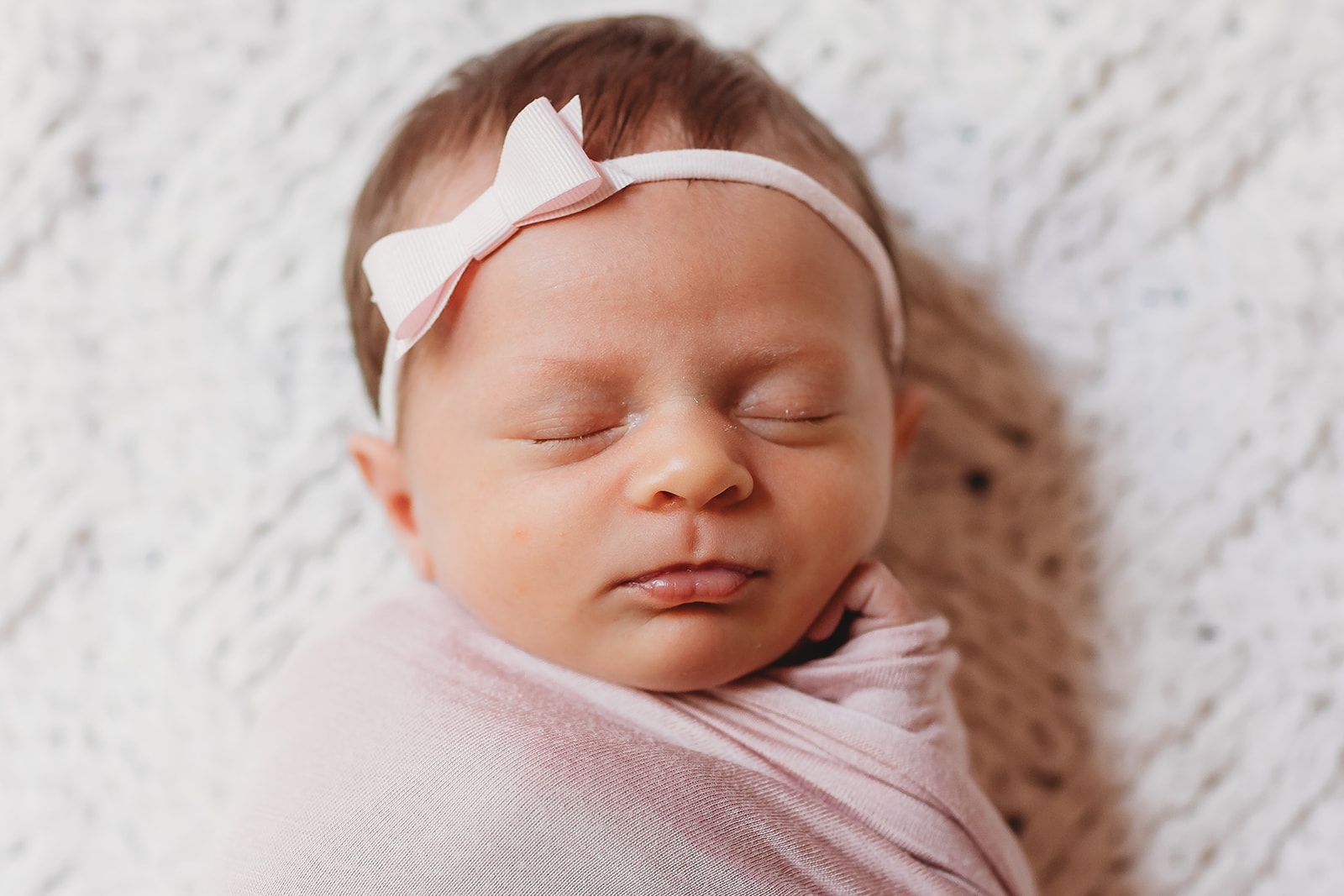 A newborn baby girl sleeps in a pink headband on a bed thanks to Brookhaven Birth Center