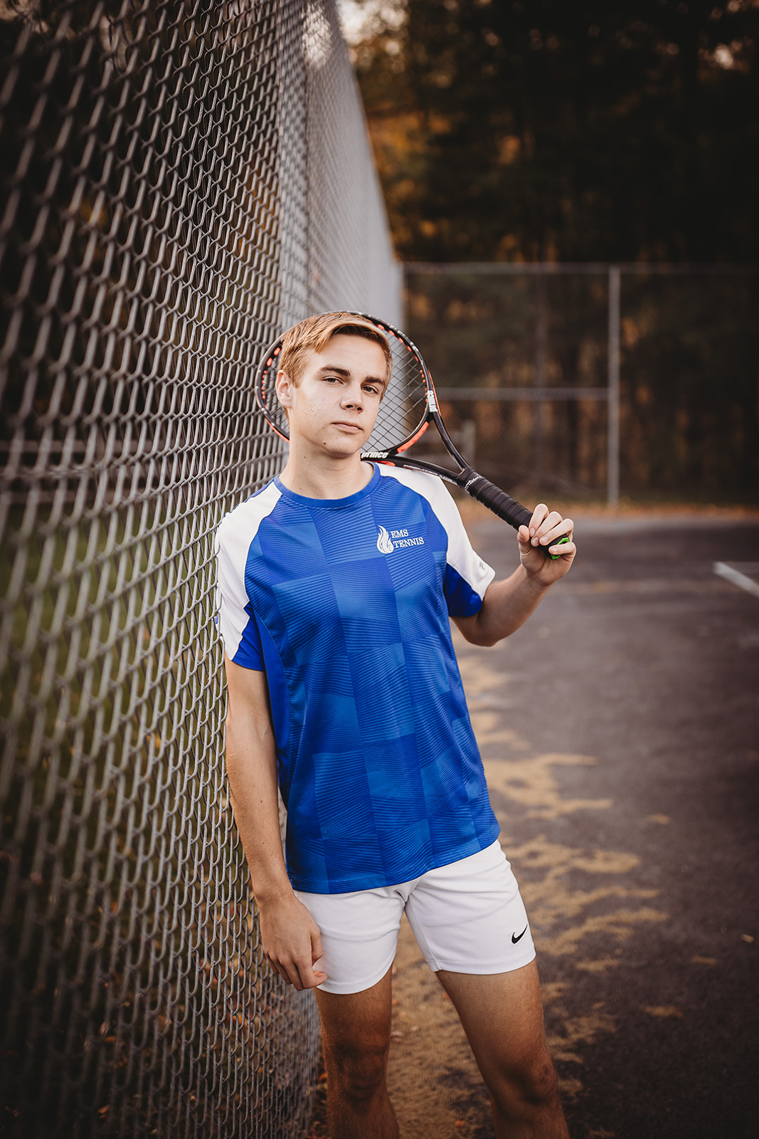 A tennis player leans on a chain link fence holding a racket in a blue shirt after exploring Colleges Near Harrisonburg, VA