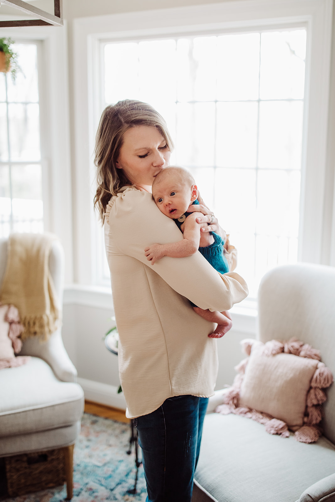 A happy mom kisses the head of her newborn baby against her chest in a living room