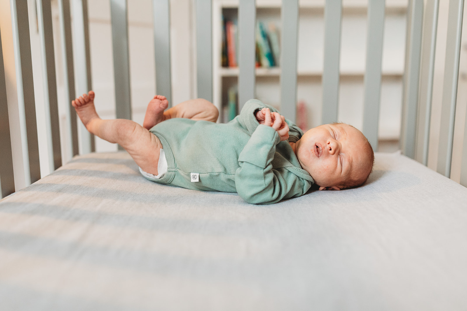 A newborn abby sleeps in a crib in a green onesie after help from Genesis Midwifery