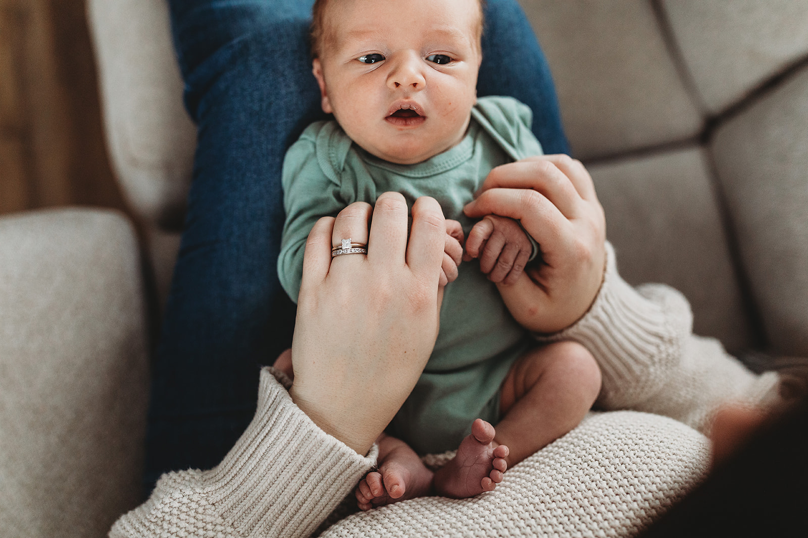 A newborn baby lays in mom's lap while holding her hands