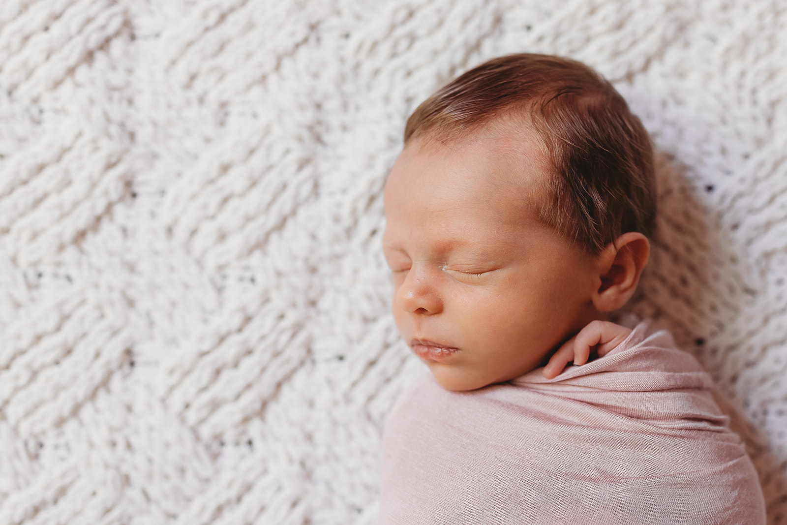 A newborn baby girl sleeps in a pink swaddle on a white blanket