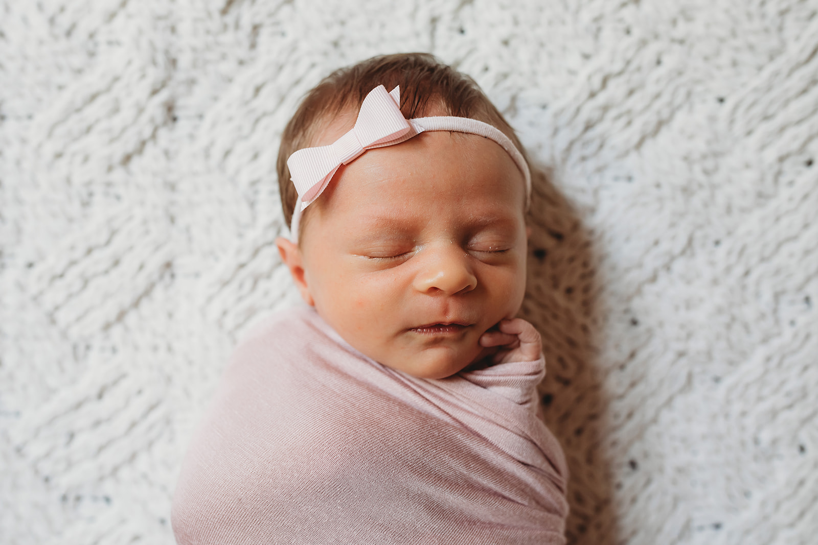 A newborn baby girl sleeps in a pink swaddle and bow on a woven blanket after meeting Midwives Harrisonburg, VA