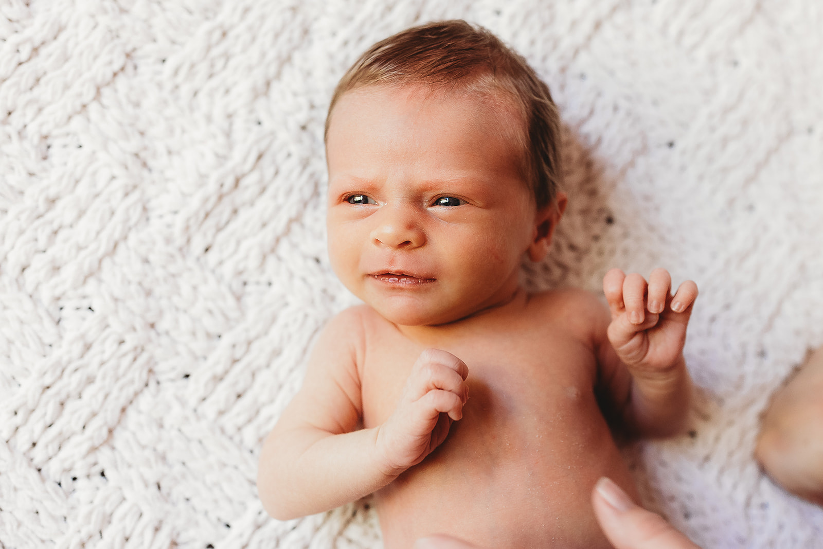 A newborn baby look up while laying on a woven blanket with no shirt thanks to Midwives Harrisonburg, VA