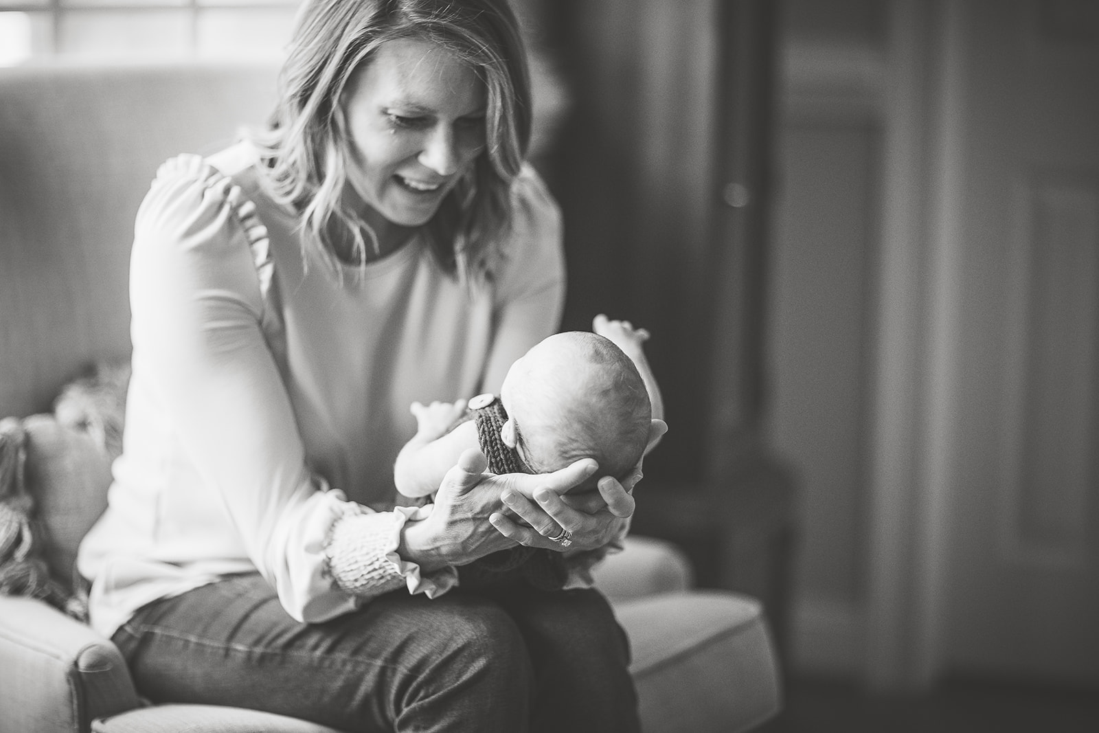 A happy new mother sits on a chair smiling down at her newborn baby in her lap thanks to an OBGYN Harrisonburg, VA