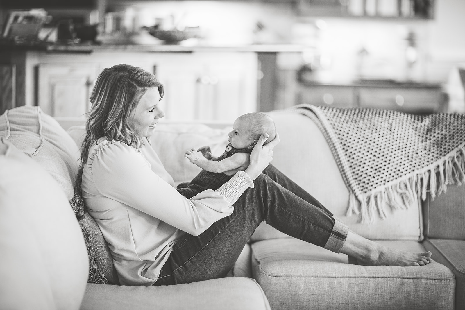 A happy mom plays with her newborn baby in her lap while sitting across a couch thanks to OBGYN Harrisonburg, VA