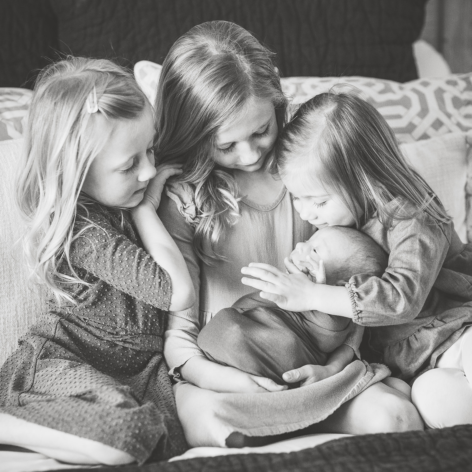 three toddler sisters admire their newborn baby sibling in their laps on a bed after visiting OBGYN Harrisonburg, VA