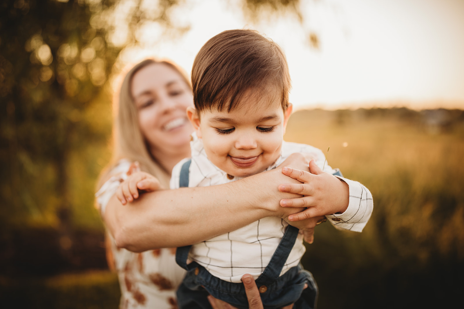 A happy toddler in held by mom while exploring a park at sunset in blue suspenders thanks to Parenting Classes in Harrisonburg, VA