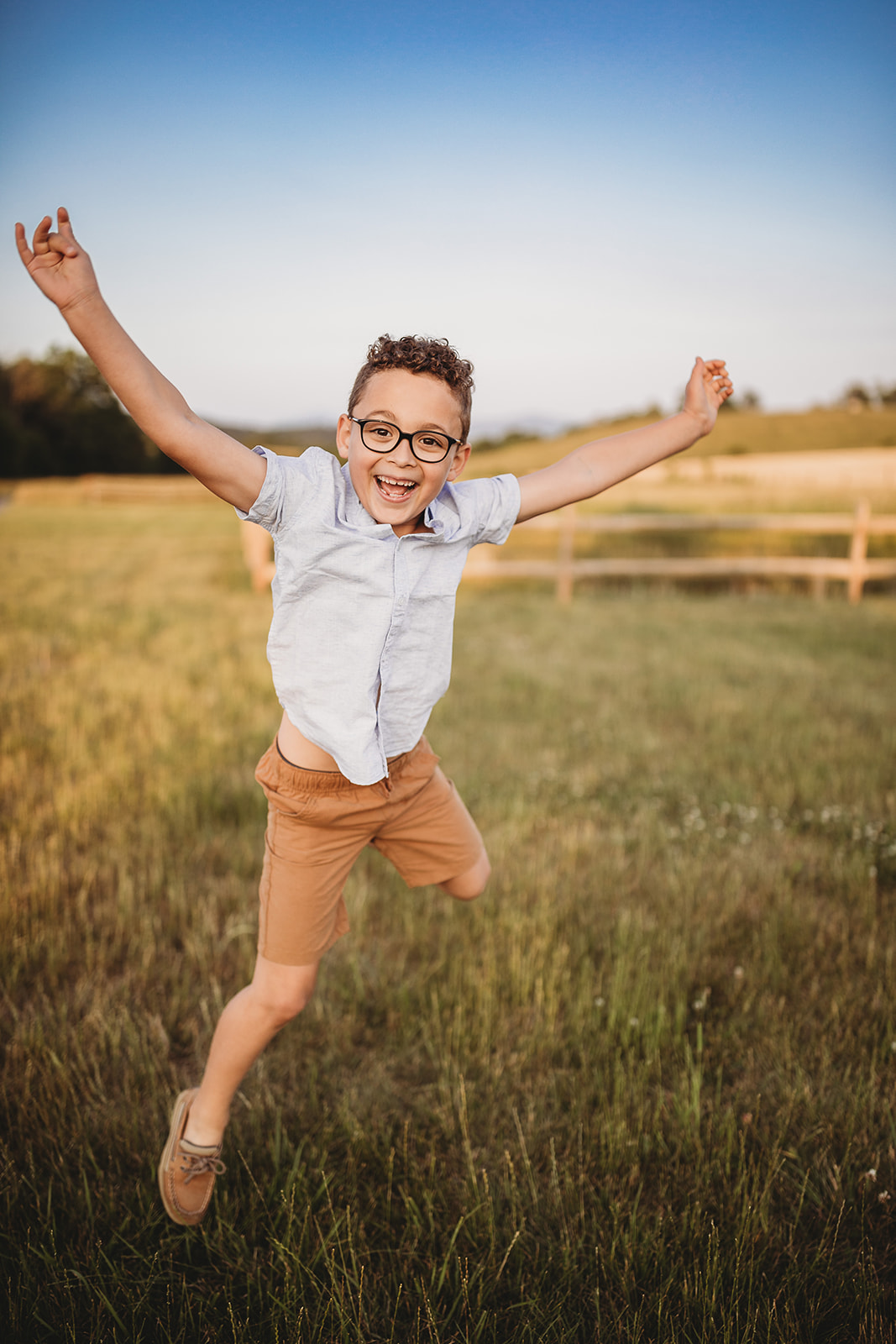 A happy young boy with glasses and a blue shirt jumps in a pasture at sunset thanks to Parenting Classes in Harrisonburg, VA