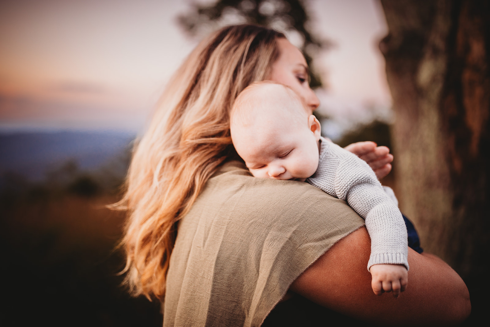 A newborn baby sleeps on mom's shoulder while exploring a park after visiting Pediatricians Harrisonburg, VA