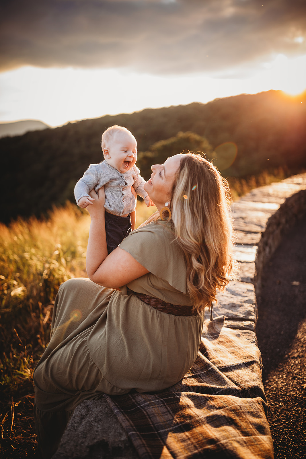 A happy infant laughs while playing with mom on a stone wall overlook at sunset after meeting Pediatricians Harrisonburg, VA