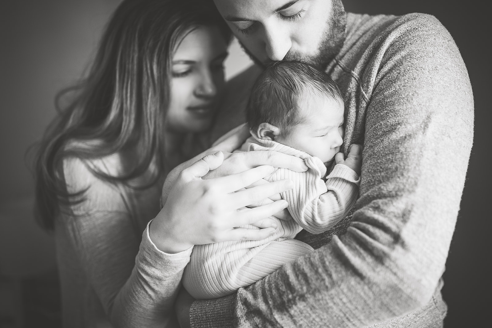 A new father kisses his sleeping newborn baby in his arms after mom had a Prenatal Massage Harrisonburg, VA