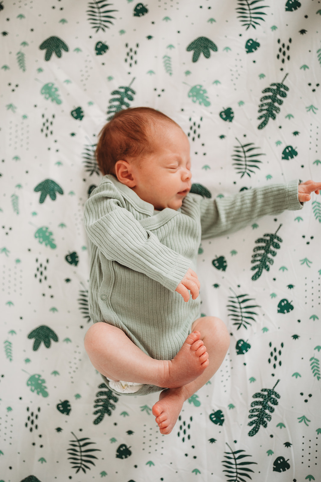 A newborn baby sleeps in a green onesie on a forest theme crib blanket after using RMH Family Birthplace