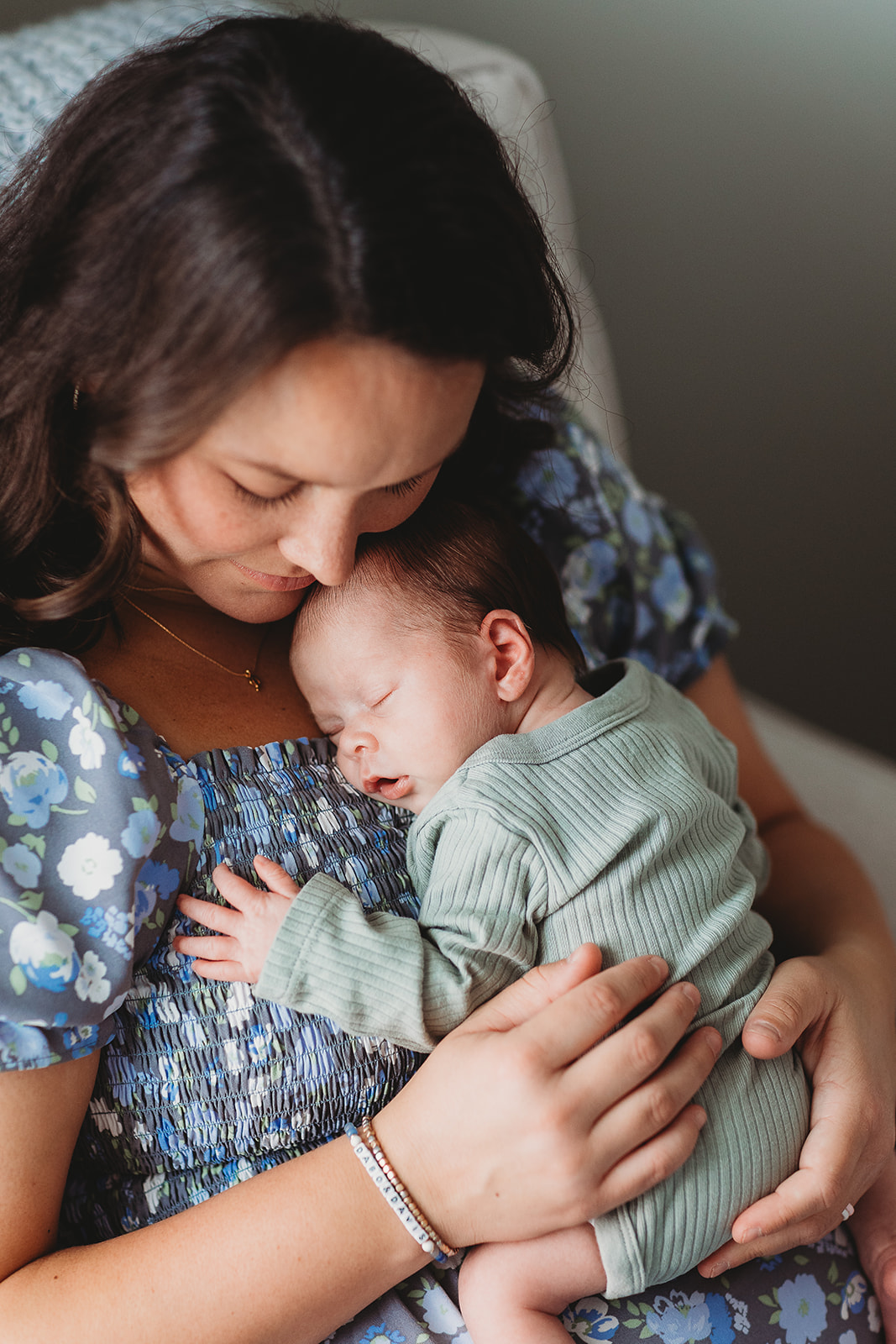 A new mom snuggles her sleeping newborn against her chest while sitting in a chair