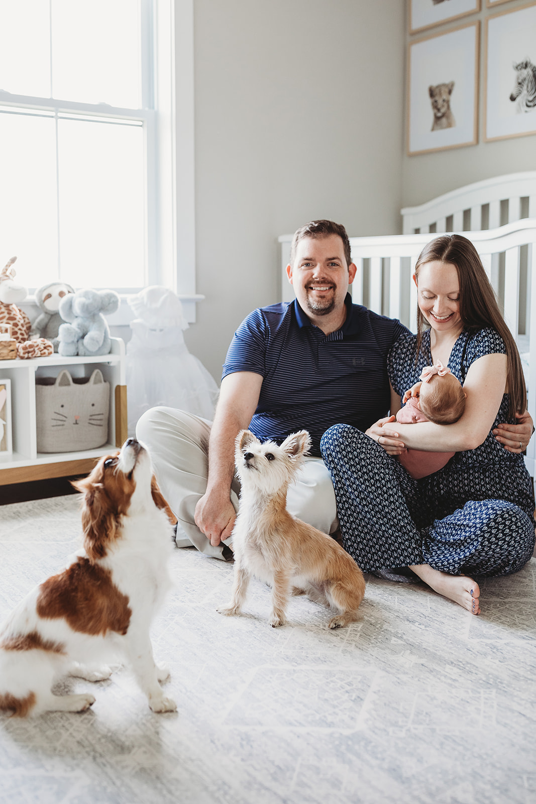 Happy new parents sit in a nursery with their newborn baby in mom's arms while their dogs sit with them thanks to Shenandoah Women's Healthcare