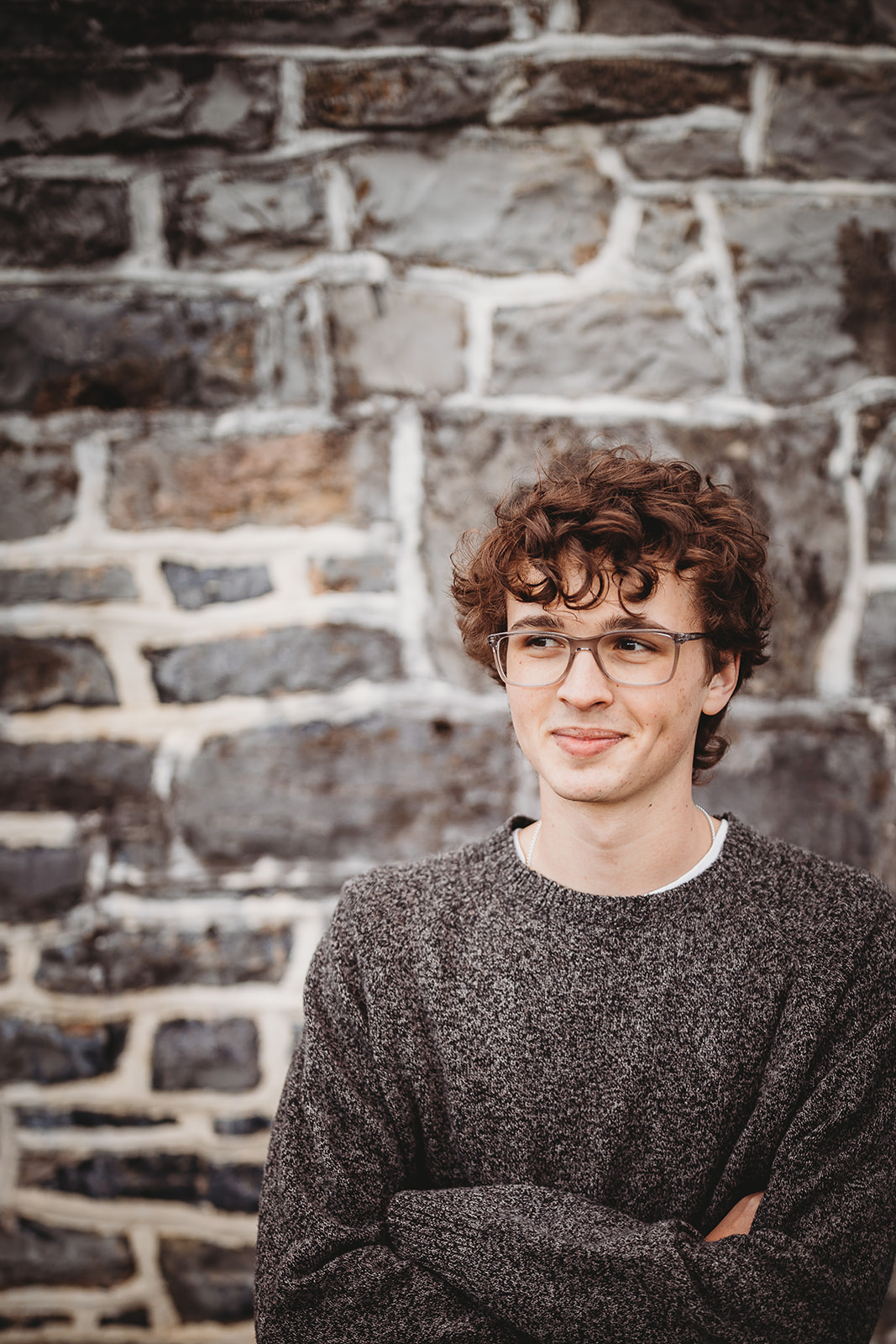 A high school senior crosses his arms while standing by a stone wall after finding Tuxedo Rental Harrisonburg, VA