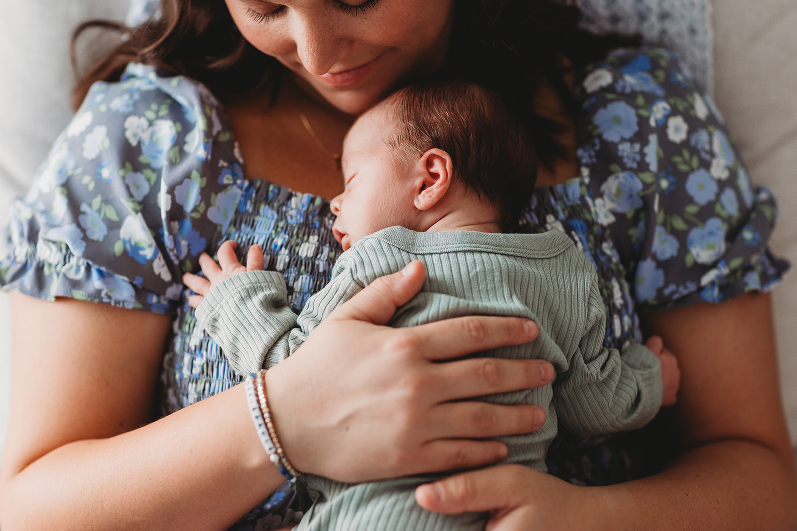 A newborn baby sleeps against mom's chest in a window in a chair