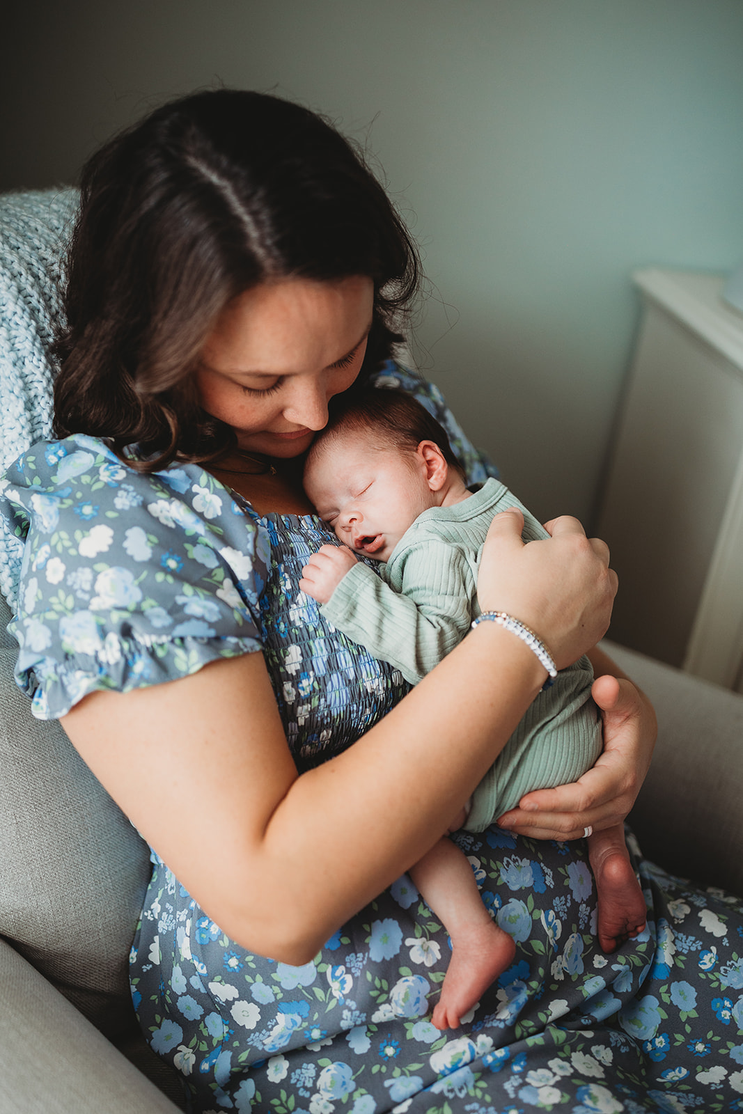 A new mom sits in a chair snuggling her newborn baby on her chest thanks to Virginia Fertility and IVF