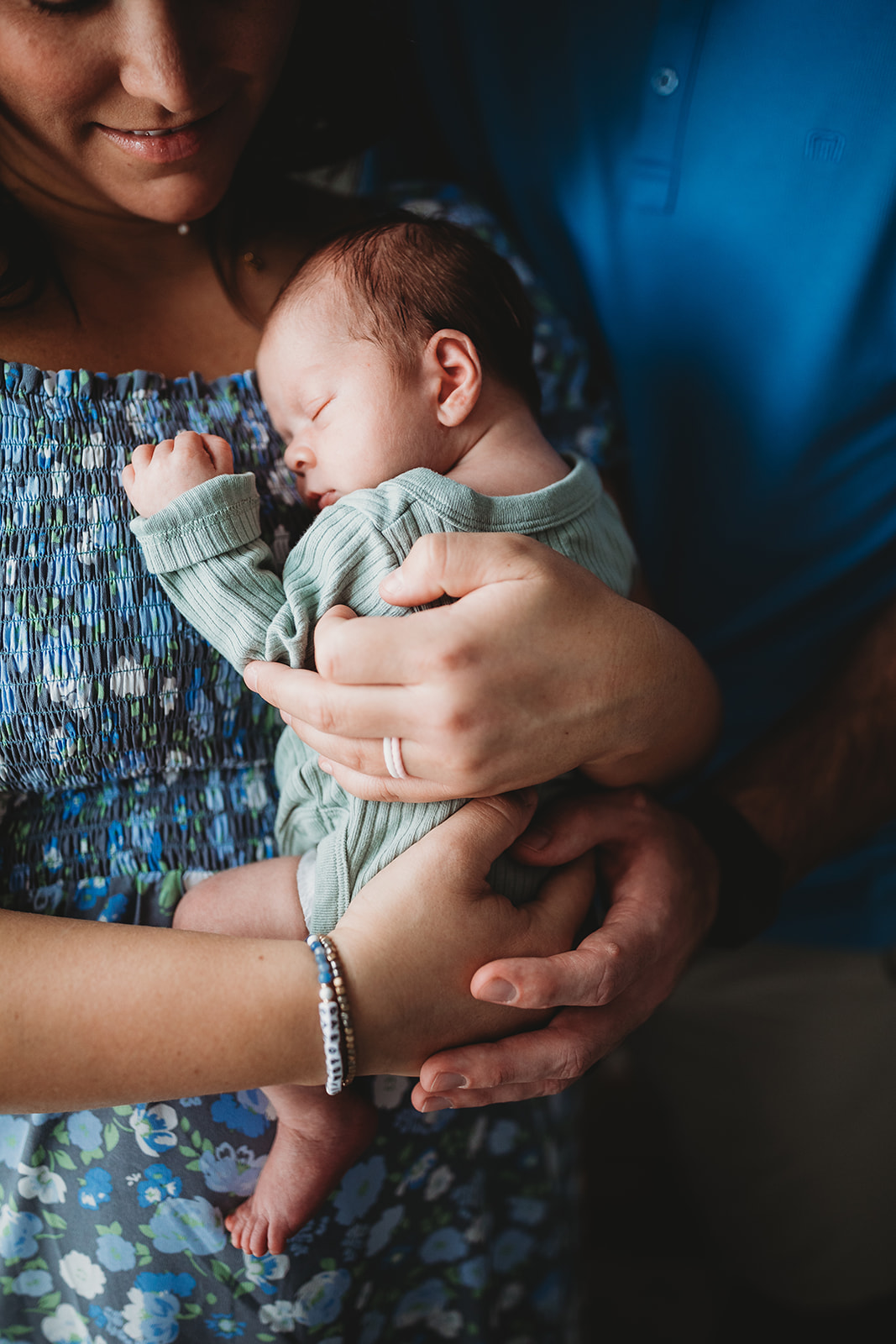 A newborn baby sleeps against mom's chest while standing in a window