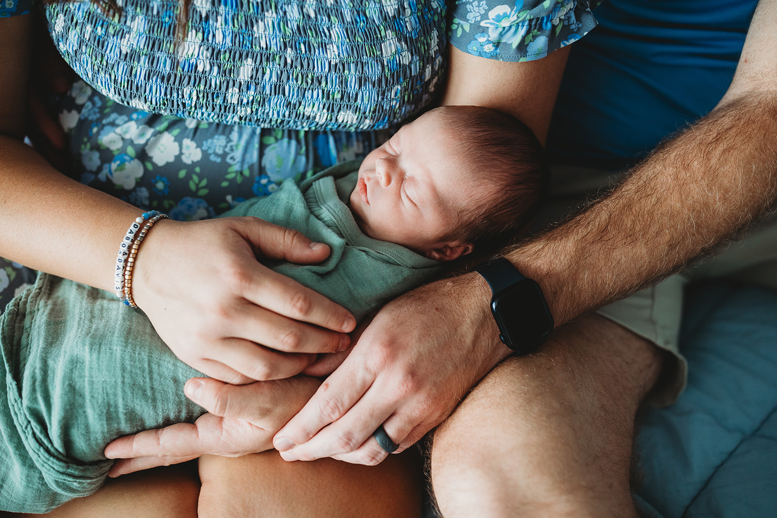 A newborn baby sleeps in a green swaddle in mom and dad's laps after they visited a Chiropractor In Harrisonburg, VA