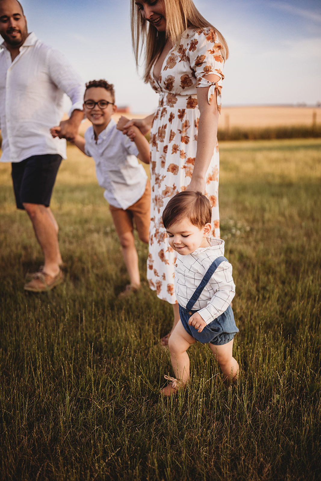 A mom and dad walk through a pasture with their toddler children holding hands after visiting EMU Musikgarten