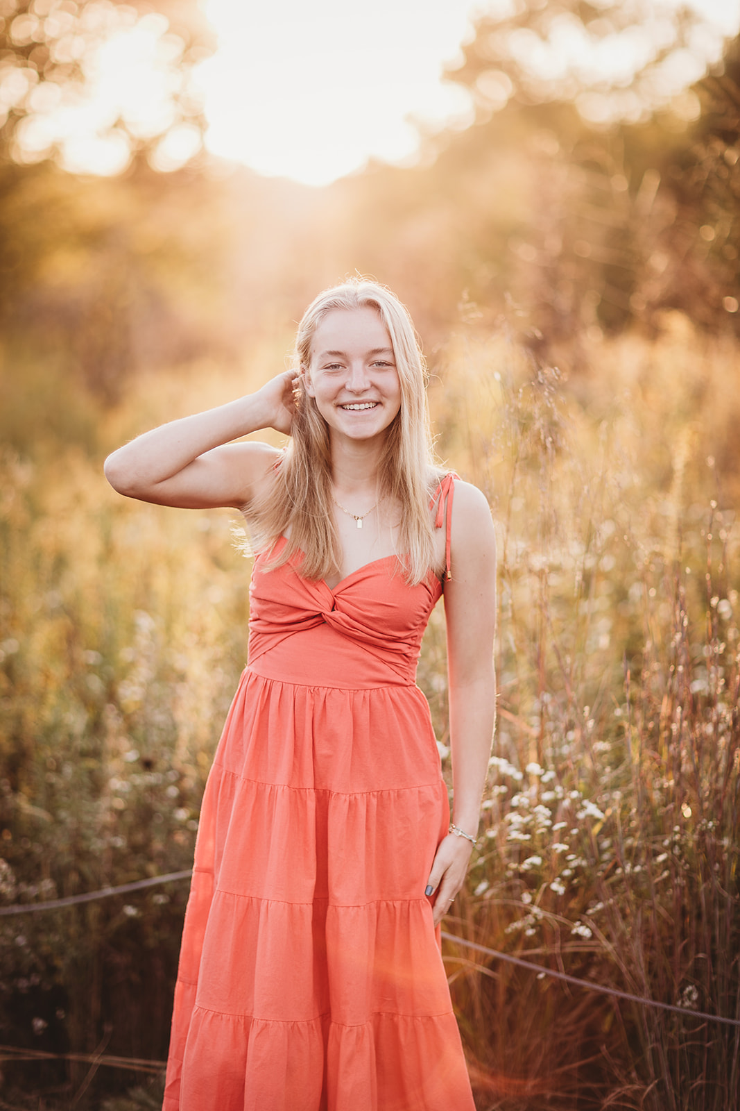 A high school senior laughs while holding her hair back in a field of tall grass