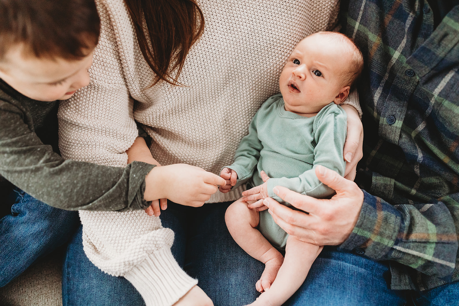 A newborn baby lays in mom and dad's lap while big brother reaches in