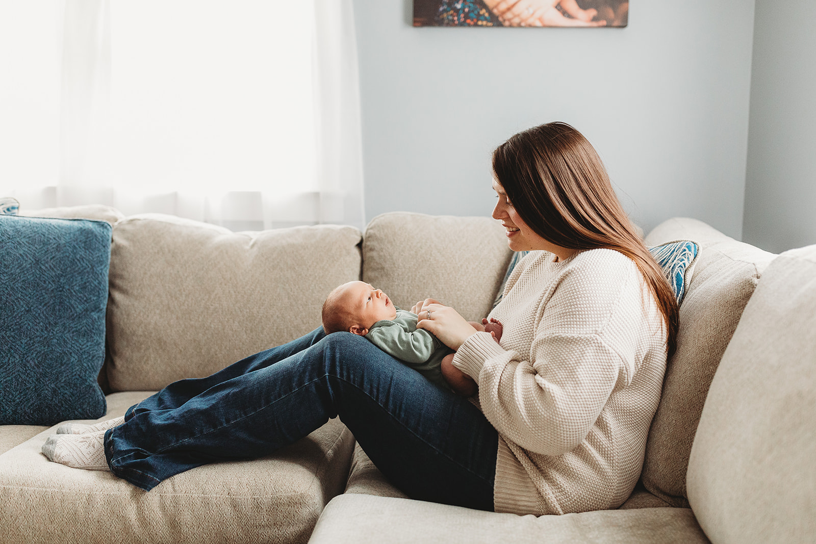 A happy mom plays with her newborn baby laying in her lap on a couch after some Pelvic Floor Therapy In Harrisonburg, VA