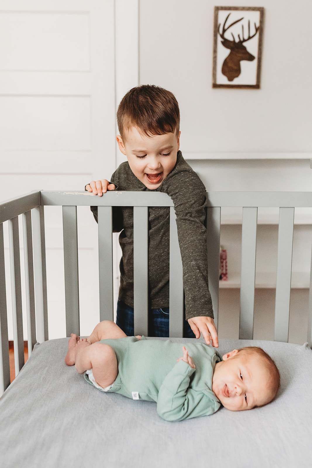 A toddler bow reaches down to his infant baby brother in a crib while mom finds Pelvic Floor Therapy In Harrisonburg, VA