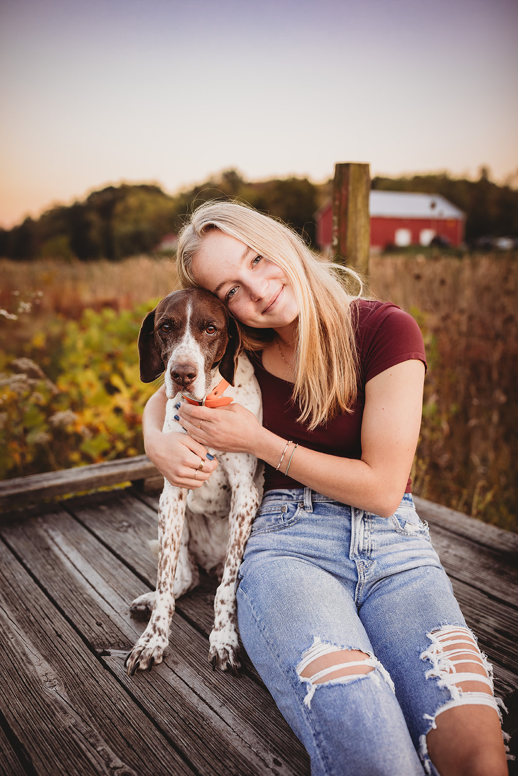 A high school senior sits on a dock hugging her brown and white dog