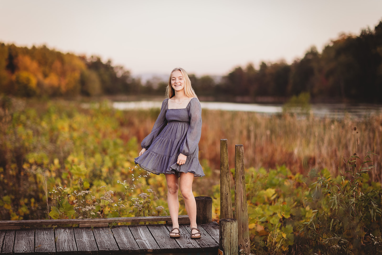 A high school senior in a grey dress dances on a wooden dock at sunset after some Tanning Harrisonburg, VA