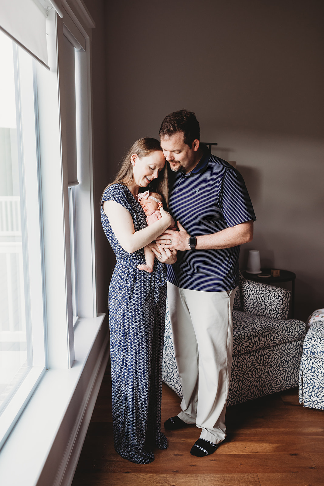 Happy new parents snuggle their newborn baby while standing in a window after some Harrisonburg Yoga