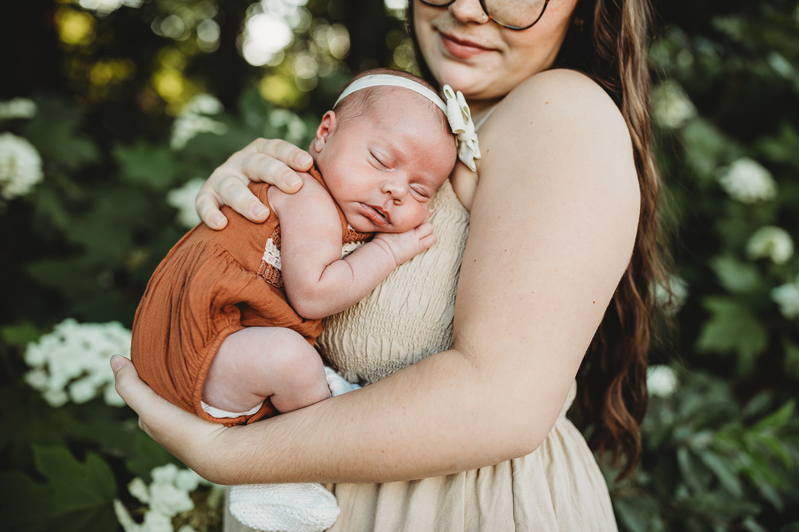 A newborn baby sleeps against mom's chest while standing in a flower garden at sunset after some placenta encapsulation in Harrisonburg, VA