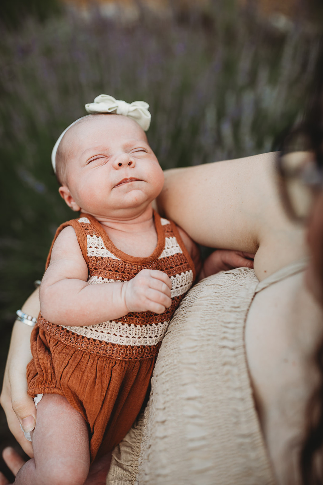 A newborn baby in an orange onesie sleeps in mom's arms in a garden after some placenta encapsulation in Harrisonburg, VA