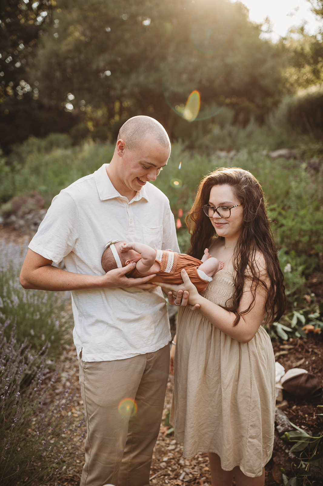 Happy new parents stand in a garden at sunset holding their infant daughter between them after some placenta encapsulation in Harrisonburg, VA